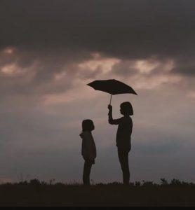 mother and child under umbrella with storm clouds overhead