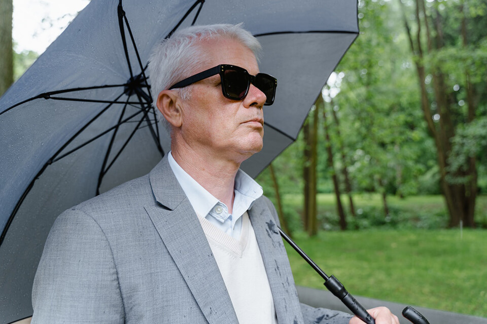 Man in a gray suit and black glasses is holding a gray umbrella
