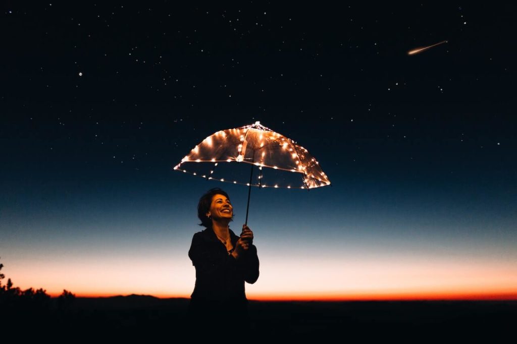Woman holding umbrella with light under the starry sky