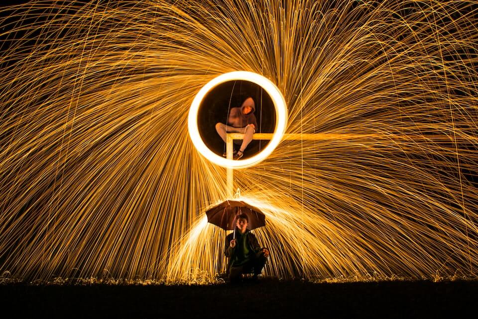 Person doing fireworks while another person sits underneath with an umbrella